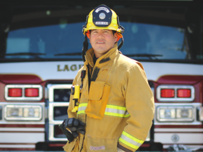 Firefighter wearing helmet and protective jacket posed in front of a fire engine
